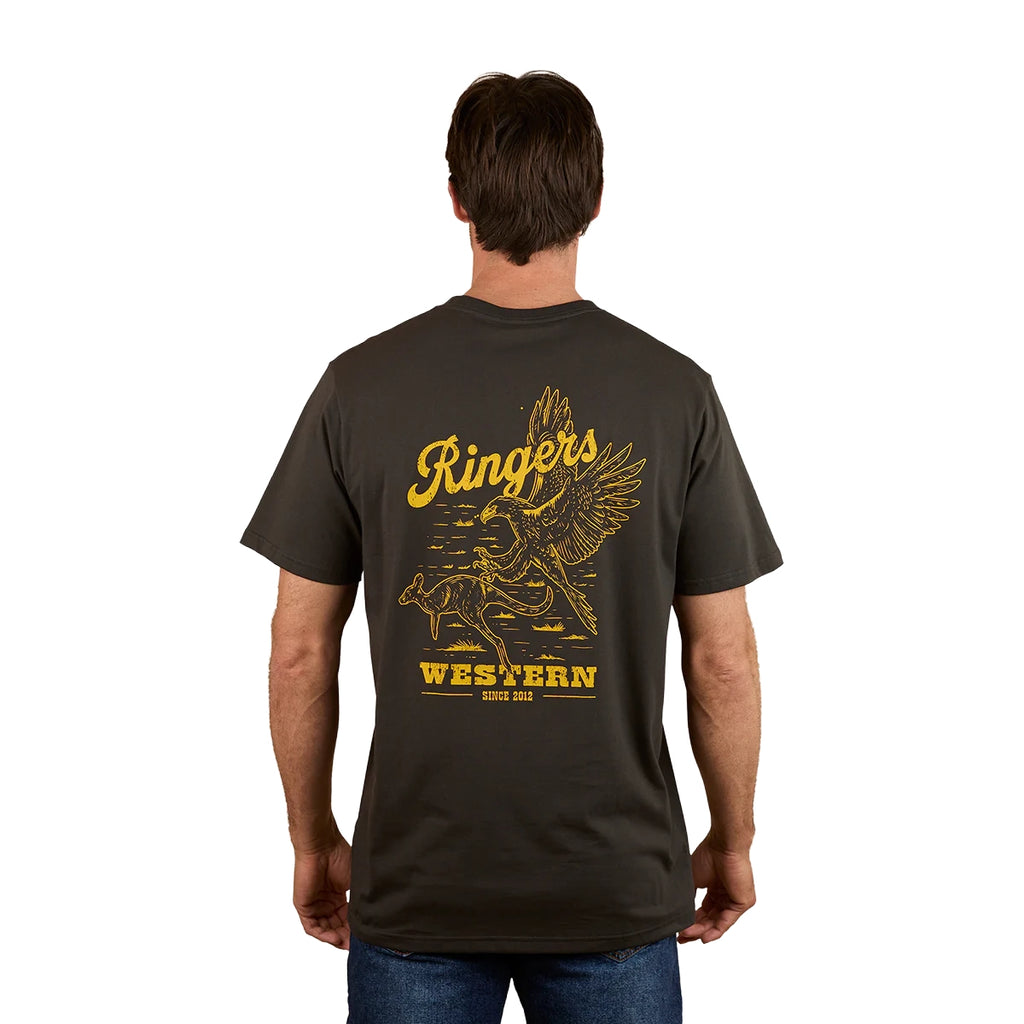 A man stands with his back to the camera wearing the Ringers Western Mens Wedge-tail Rampage Loose Fit S/S Tee in Charcoal, featuring yellow artwork of an eagle, a cowboy on a bucking bull, and "Ringers Western Since 2012.