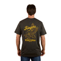 A man stands with his back to the camera wearing the Ringers Western Mens Wedge-tail Rampage Loose Fit S/S Tee in Charcoal, featuring yellow artwork of an eagle, a cowboy on a bucking bull, and "Ringers Western Since 2012.