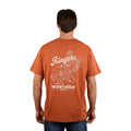 A man, facing away, wears a Ringers Western Mens Wedge-tail Rampage Loose Fit S/S Tee in rust with a white graphic of a winged cowboy on horseback and “Ringers Western Since 2012.”.