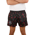 A person wearing a white t-shirt and Ringers Western Unisex Rose Of The Desert Footy Shorts in black with a red floral pattern and circular white logo on the left leg stands with arms crossed. Photo cropped at shoulders and mid-thigh.