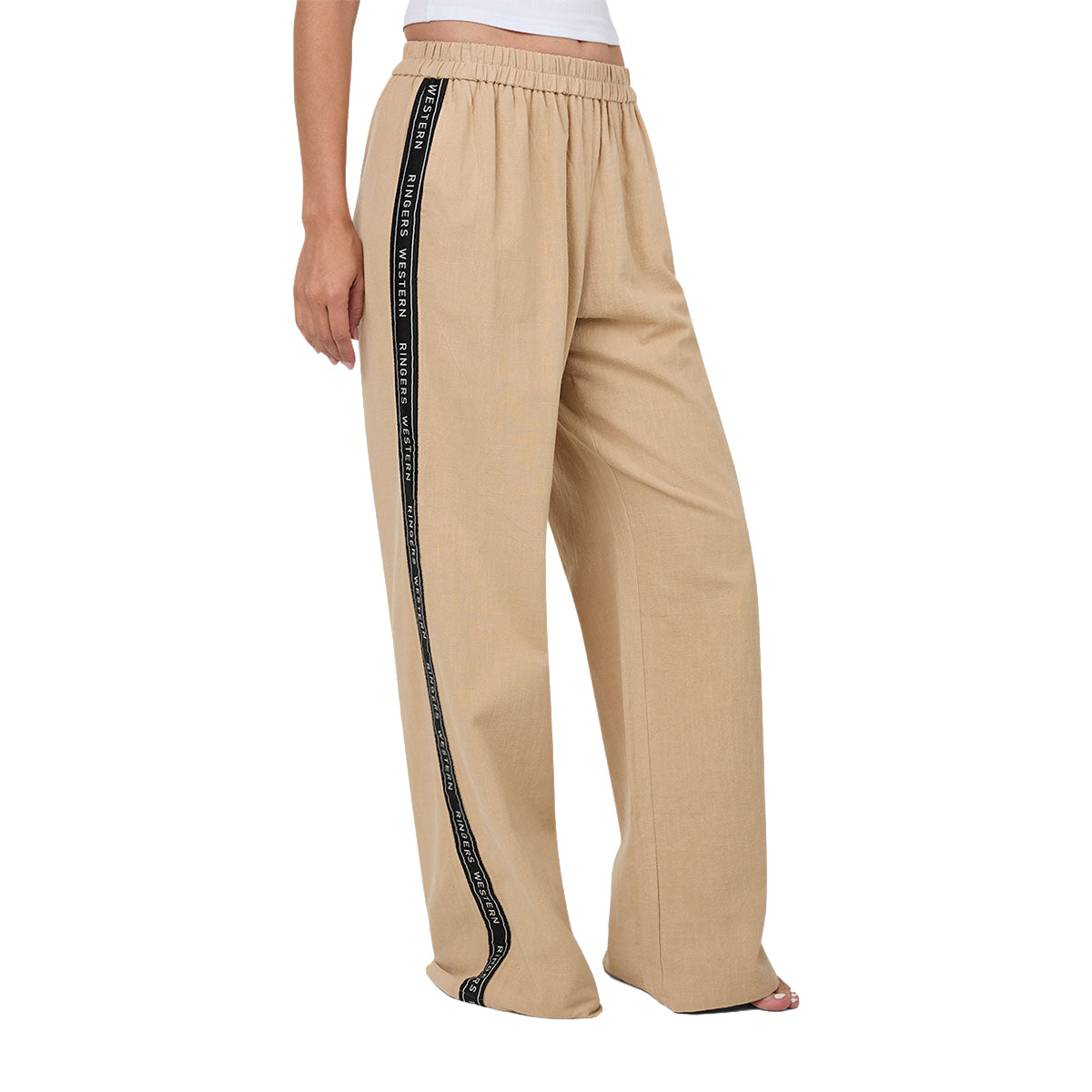 A woman from 3-4 front wearing beige Ringers Western Alexis Elastic Waist Wide Leg Pants (225045RW) with a black side stripe featuring Ringers Western text, shown from the waist down against a plain white background.