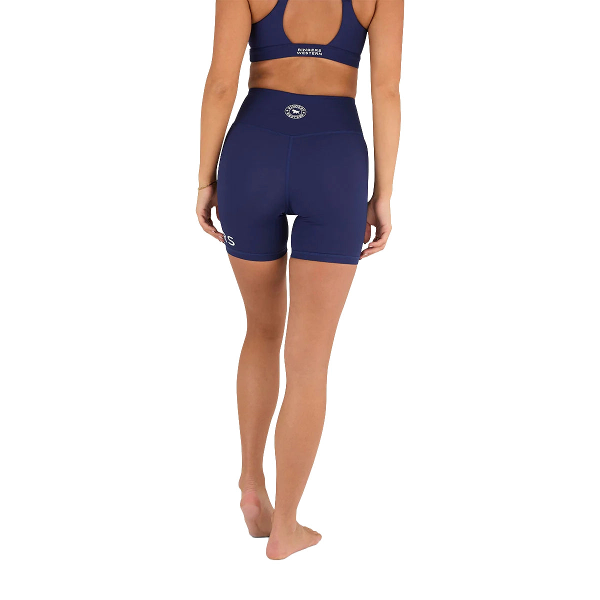 A person wearing Ringers Western Womens Anikafit Signature Shorts (225012RW) Midnight stands barefoot, facing away from the camera against a plain white background. The high-waisted shorts are squat-proof for confident movement.