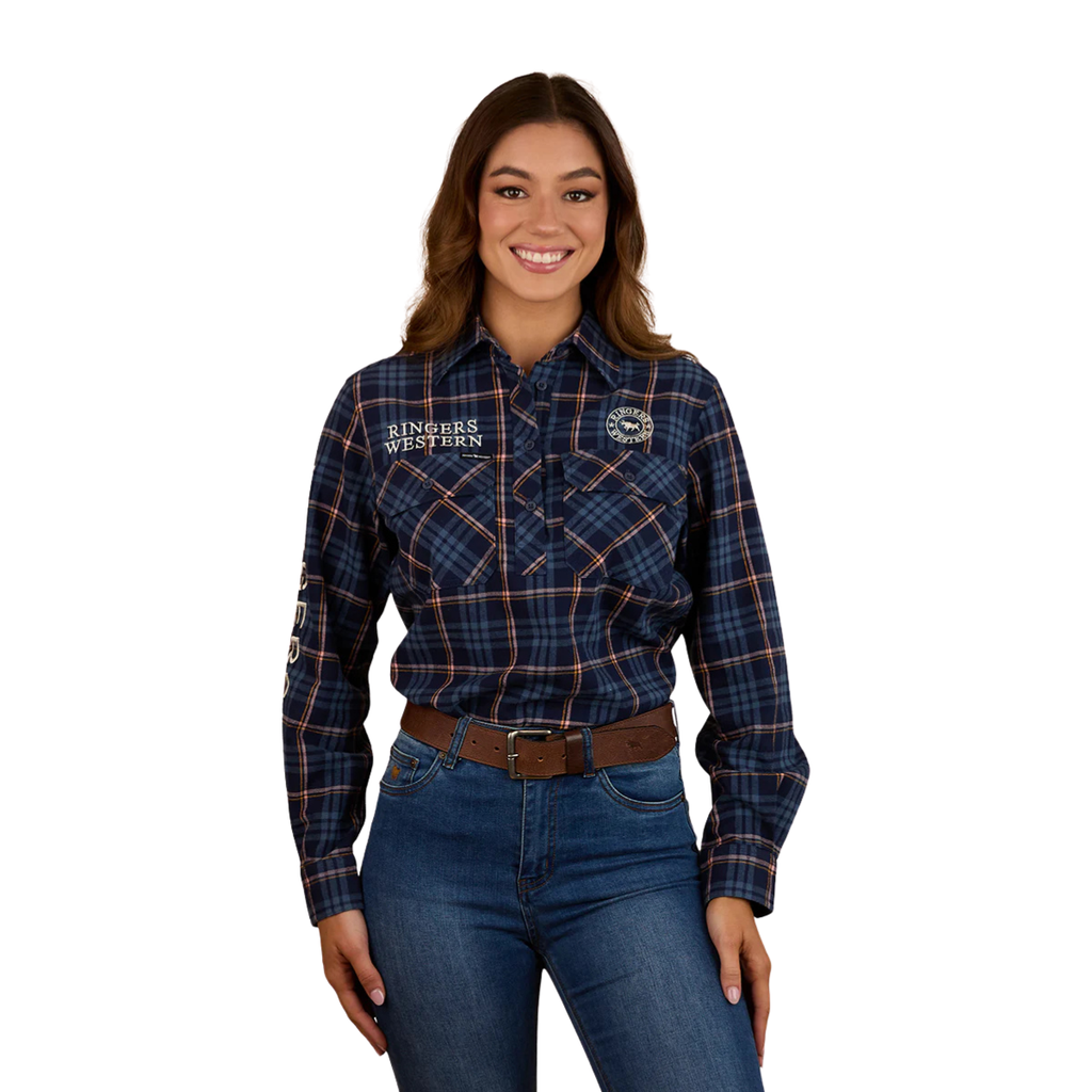 A woman with long brown hair smiles in a Ringers Western Womens Fingal Half Button L/S Flannel Shirt (224016RW) Dark Blue, paired with jeans and a brown belt—authentic Australian country style against a white background.