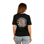 A woman with light brown hair wears the Ringers Western Womens Outta Towner Loose Fit S/S Tee in black, featuring a colorful lion crest and "Ringers Western" on the back, paired with light blue jeans for an Aussie-inspired look.