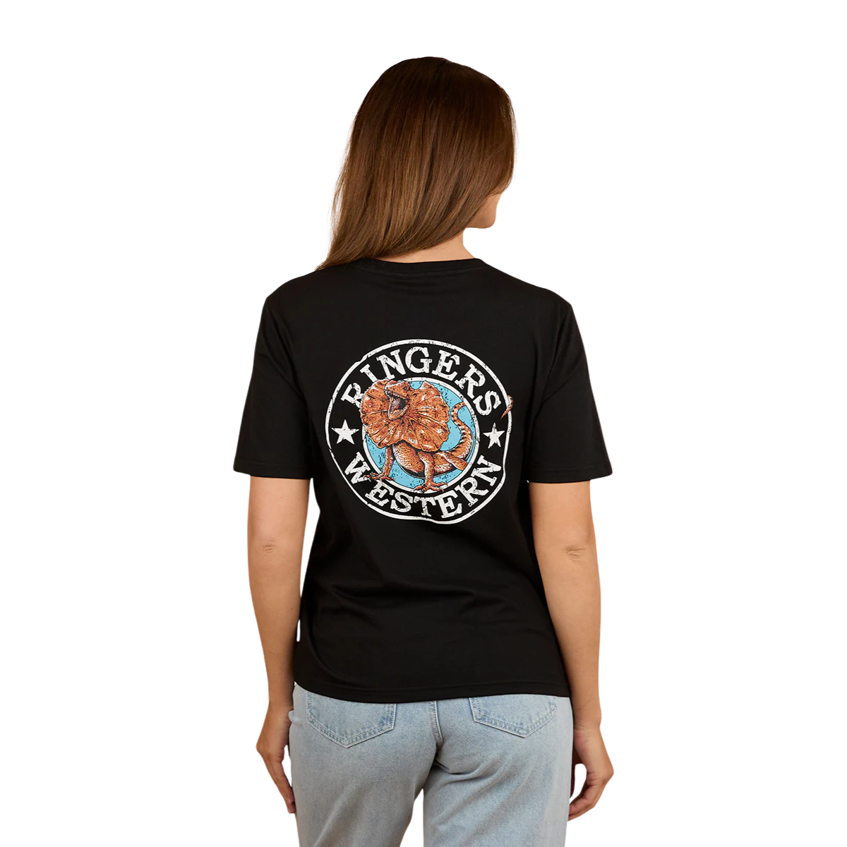 A woman with light brown hair wears the Ringers Western Womens Outta Towner Loose Fit S/S Tee in black, featuring a colorful lion crest and "Ringers Western" on the back, paired with light blue jeans for an Aussie-inspired look.