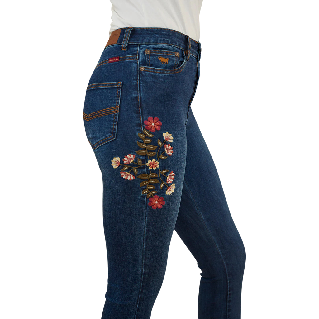 A close up of a woman wearing classic blue Ringers Western Women's Penny Rodeo High Rise Bootleg Jeans (222104RW) showing colourful floral embroidery on the right side thigh, against a plain white background.