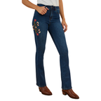 A woman wearing classic blue Ringers Western Women's Penny Rodeo High Rise Bootleg Jeans (222104RW) showing colourful floral embroidery on the right side thigh, paired with brown leather boots against a plain white background.