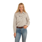 A woman with long blonde hair smiles against a white background, wearing the Ringers Western Womens Pentecost River Half Button L/S Work Shirt in beige and blue jeans, with one hand in her pocket.