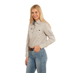 A woman with long blonde hair smiles against a white background, wearing the Ringers Western Womens Pentecost River Half Button L/S Work Shirt in beige and blue jeans, with one hand in her pocket.