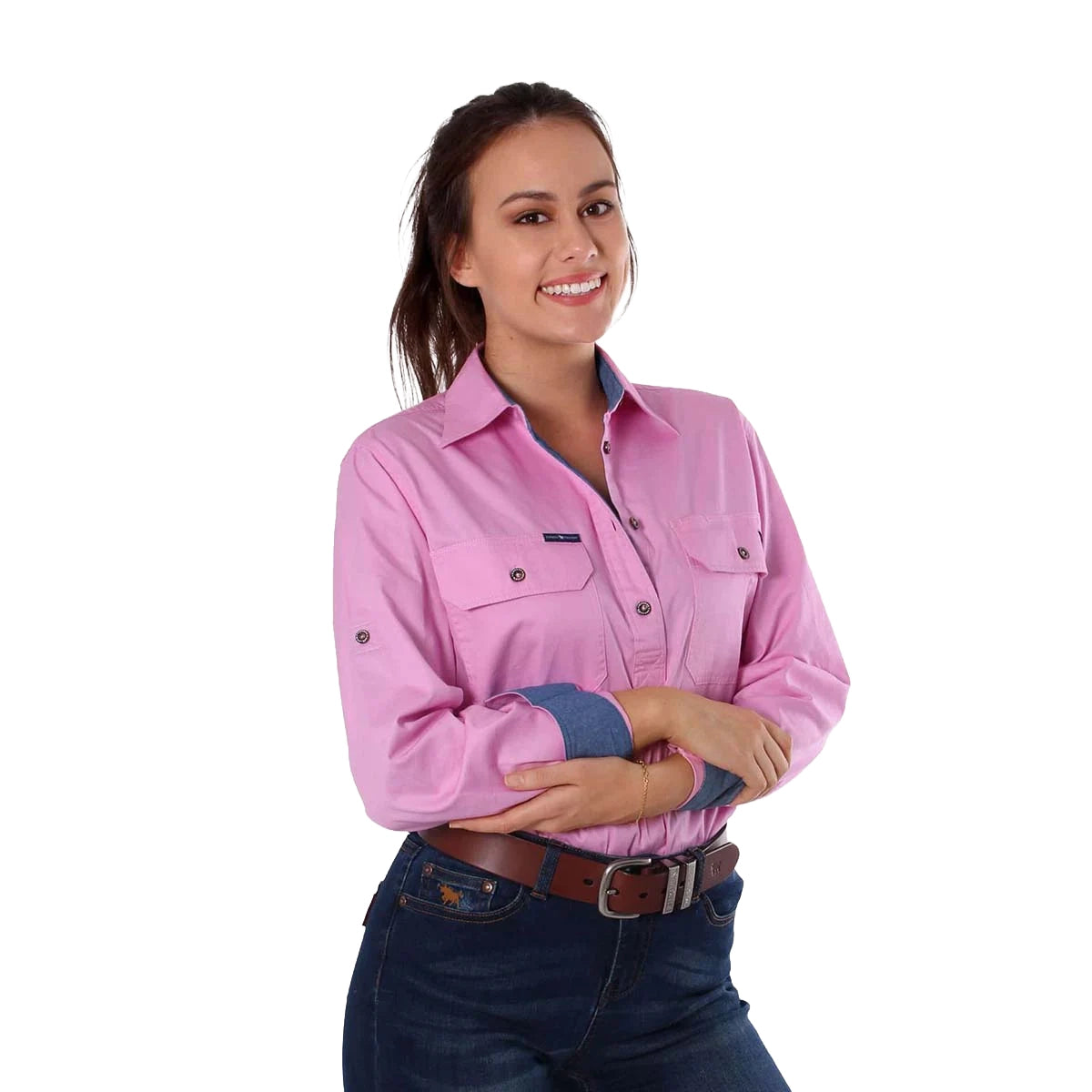 A woman with long brown hair smiles, arms crossed, wearing a Ringers Western Womens Pentecost River Half Button L/S Work Shirt in pastel pink and blue jeans against a white background.