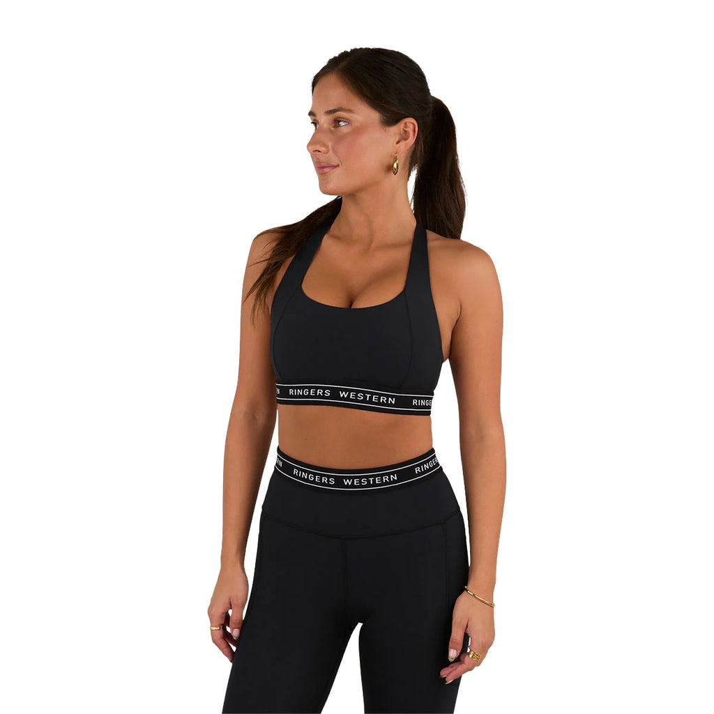 A woman wearing the Ringers Western Womens Ringers Active Logo Elastic Support Crop Top (225009RW) in black stands against a white background, looking left with her hair in a ponytail.