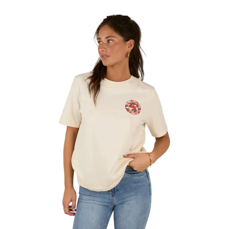 A woman in the Ringers Western Womens Signature Bull Loose Fit S/S Tee in Off White/Cow Print and blue jeans stands with one hand in her pocket, looking to her left.