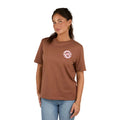A woman wears the Ringers Western Womens Signature Bull Loose Fit S/S Tee in Saddle Brown/Cow Print with light blue jeans, smiling softly against a plain white background.