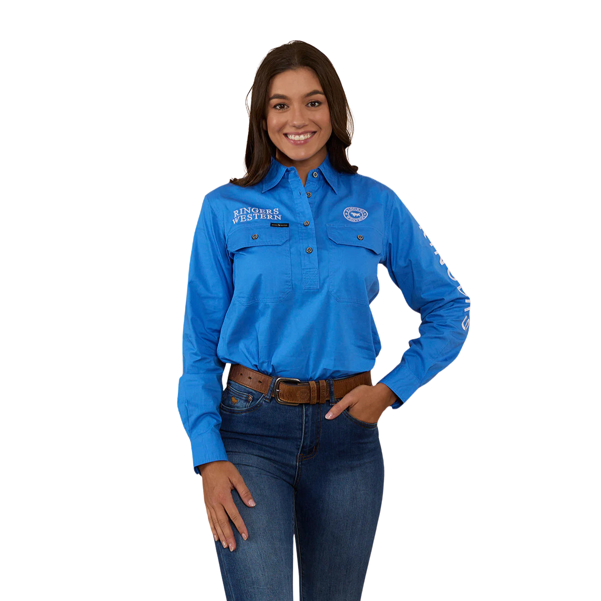 A woman smiles with one hand in her pocket, wearing a Ringers Western Womens Signature Jillaroo Half Button L/S Work Shirt (223125RW) in blue, dark jeans, and a brown belt against a white background.