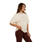 A woman with long brown hair smiles, wearing the Ringers Western Womens Stampede Oversized S/S Tee (225074RW) in Bone. She pairs it with dark brown pants and stands against a plain white background, one hand on her hip.