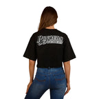 A woman wearing a Ringers Western Womens Twilight Oversized Cropped S/S Tee (225059RW) in black, paired with blue jeans and a black belt, smiles while standing against a plain white background.