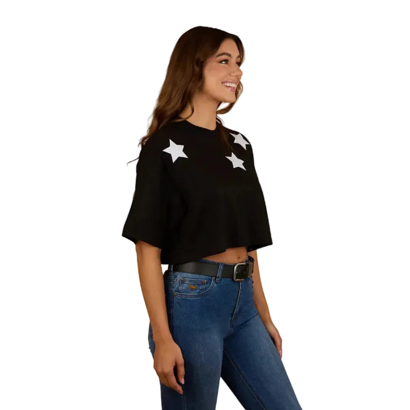 A woman wearing a Ringers Western Womens Twilight Oversized Cropped S/S Tee (225059RW) in black, paired with blue jeans and a black belt, smiles while standing against a plain white background.