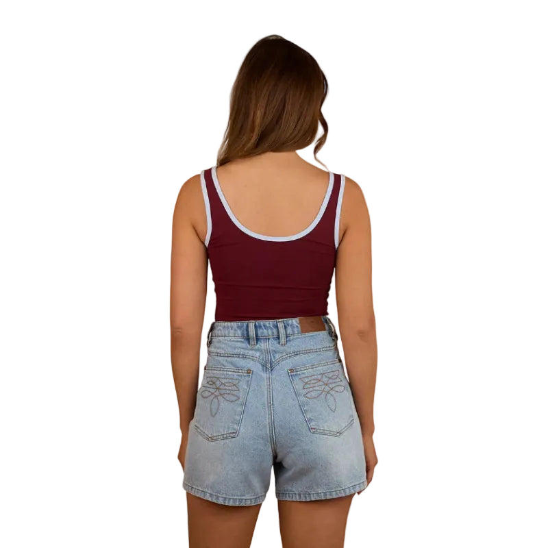 A woman faces away, wearing a Ringers Western Womens Villa Ringer Tank in Burgundy/Light Blue and light denim shorts with embroidered back pockets, set against a white background.