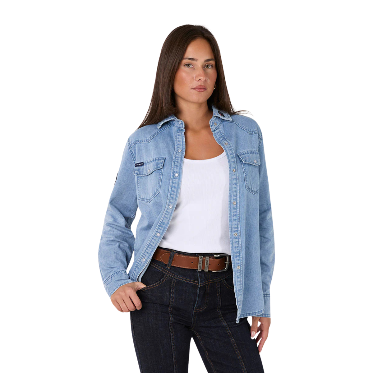 A woman wears the Ringers Western Womens Young and Free L/S Western Shirt in Light Wash Blue over a white tank, paired with dark jeans and a brown belt, standing with one hand in her pocket against a plain white background.