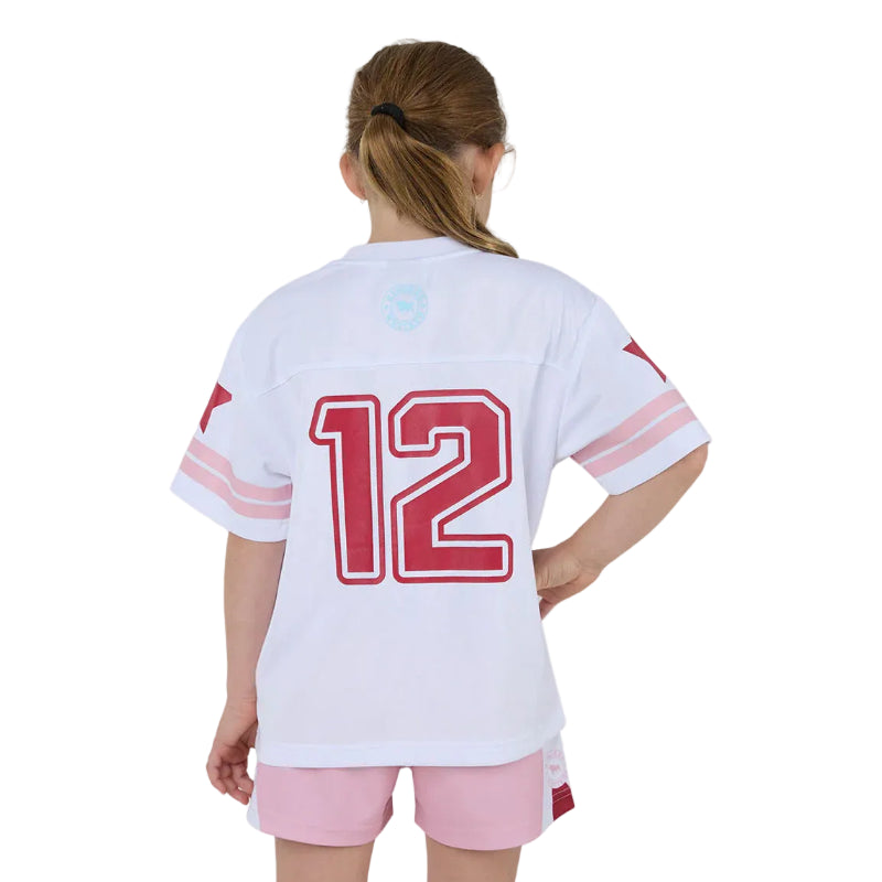 A child model shown from the back wearing a white short-sleeve sports jersey with pink sleeve stripes and a large red number 12 on the back, paired with light pink shorts against a plain white background.