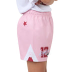 Pink athletic shorts with a red star, a white geometric graphic, and a red number 12 on the front, shown on a child wearing a white shirt against a white background.
