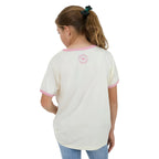 A girl from behind wearing a cream-colored ringer t-shirt with pink trim on the collar and cuffs, featuring a circular pink logo on the upper back.