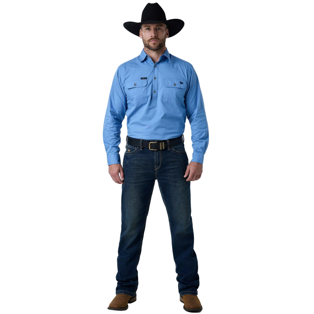 A man wearing a light blue long-sleeve western shirt, dark blue jeans, a black cowboy hat, and brown boots, standing against a white studio background.