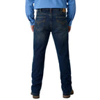 Rear view of a person wearing dark blue denim jeans with a light blue long-sleeve shirt and brown shoes, shown against a white studio background.