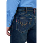 Close-up back view of a person wearing dark blue denim jeans with contrast tan stitching and a light blue button-up shirt.