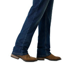 A close-up of a person's legs wearing dark blue jeans and brown suede boots against a white studio background.