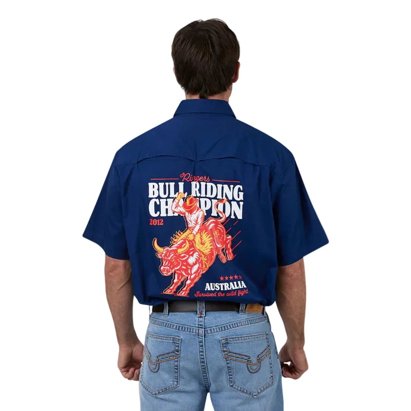 A man viewed from the back wearing a navy blue short-sleeve button-up shirt with a large red, orange, and white bull riding graphic and text on the back, paired with light blue jeans.