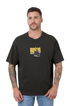 A man wearing a black short-sleeve t-shirt with a yellow and white graphic on the chest, paired with blue jeans, against a white background.