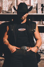 A man wearing a black cowboy hat, black sleeveless shirt, and black muscle tank with a 'Ringers Western' logo, standing in a rustic western-themed setting.