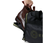 A black and army Ringers Western Rider Go Sports Bag (625130RW) duffel bag with 'Ringers' branding, featuring a top carry handle, top zipper, and a front pocket with red lettering. Shown with a hand placing brown leather Chelsea boots into its zippered end compartment.