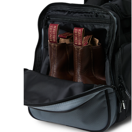 A black and charcoal Ringers Western Rider Go Sports Bag (625130RW) duffel bag with 'Ringers' branding, featuring a top carry handle and showing the zipped end compartment with a pair of brown chelsea boots in it.