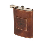 A brown leather flask cover with a silver metal flask visible at the top, featuring a stitched square patch with a logo on a white background.