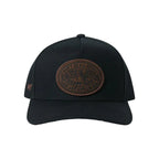 A black baseball cap featuring a prominent brown circular leather patch on the front with a small embroidered logo on the side, set against a white background.