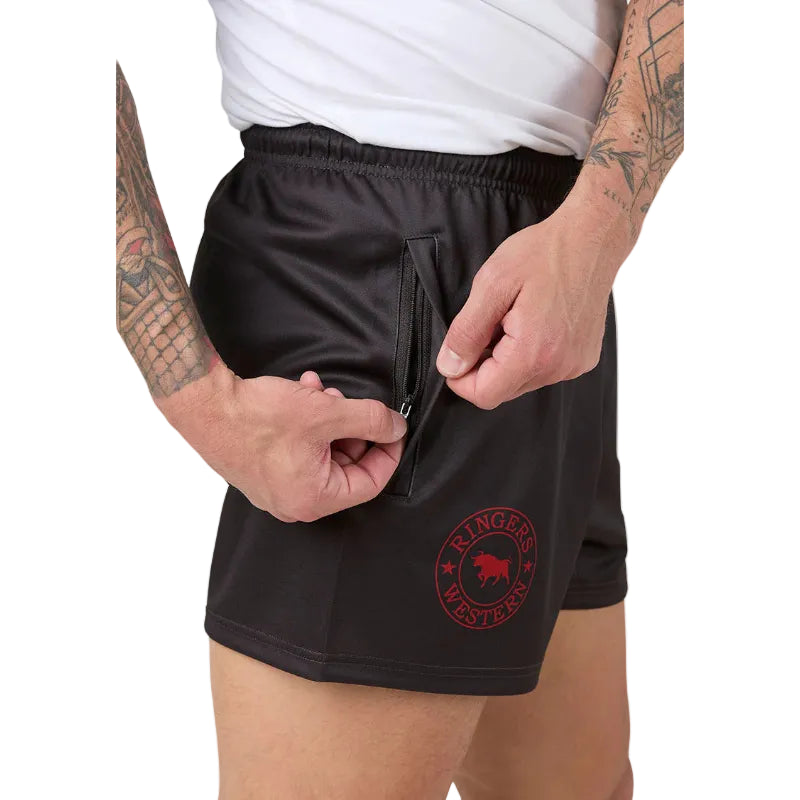 charcoal grey footy shorts with a red circular logo on the left leg, featuring a zippered side pocket, shown on a model wearing a white tee.