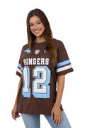 A woman wearing a brown short-sleeve football-style jersey with 'RINGERS' and the number '12' in white outlined in light blue, plus light blue sleeve stripes, against a plain light background.