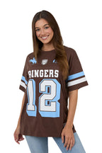 A woman wearing a brown short-sleeve football-style jersey with 'RINGERS' and the number '12' in white outlined in light blue, plus light blue sleeve stripes, against a plain light background.