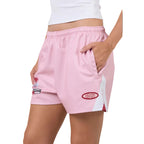 Pink footy shorts with side pockets, featuring a white side panel and embroidered logos, shown on a model against a white background.