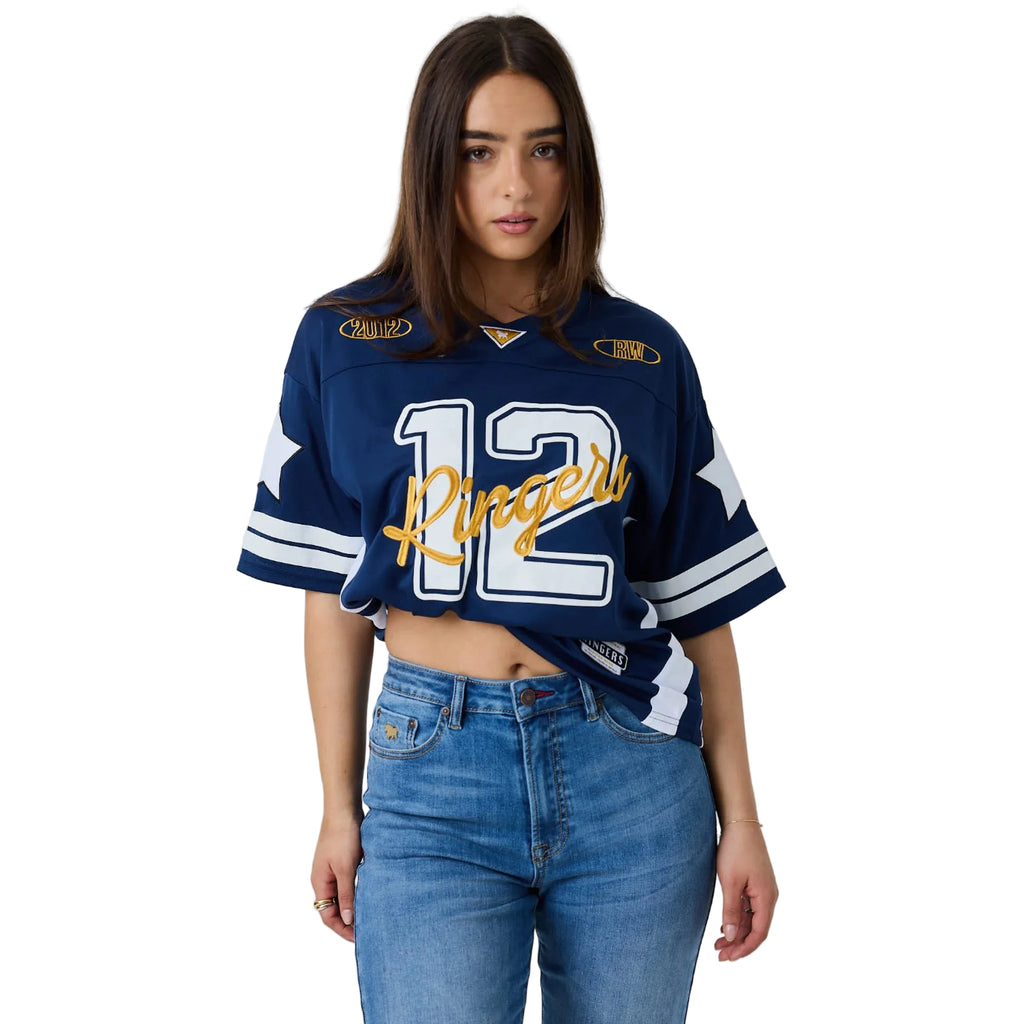 A woman modeling a navy blue cropped sports jersey with white and gold details, featuring the number 12 and the word 'Rangers' across the front, paired with blue jeans against a white studio background.