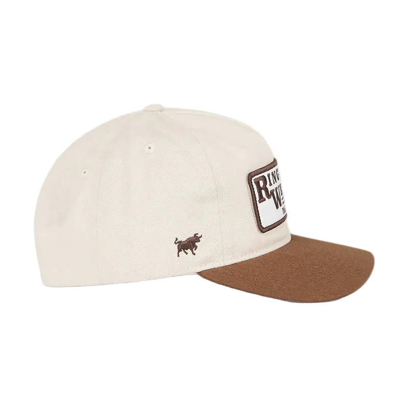 An off-white baseball cap with a brown curved brim, featuring a small embroidered brown bull logo on the side and a larger rectangular patch on the front, set against a white background.