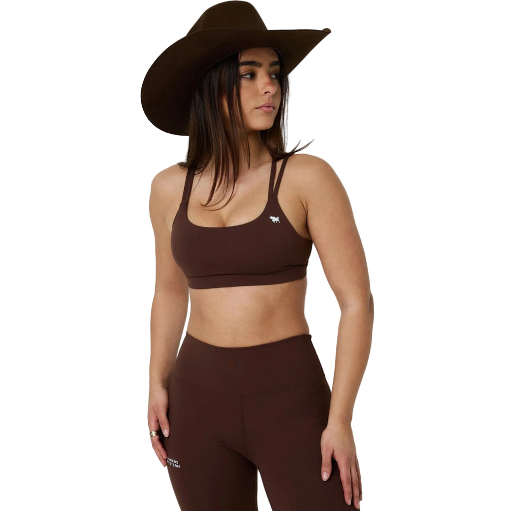 A woman modeling a matching dark brown activewear set consisting of a sports bra and high-waisted leggings, paired with a wide-brimmed brown hat, against a white studio background.