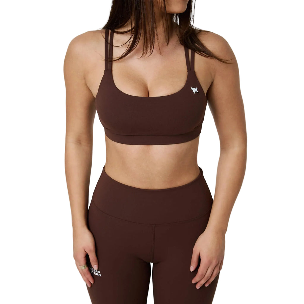 A woman wearing a matching brown activewear set consisting of a scoop-neck sports bra and high-waisted leggings, shown from the chest down against a white  studio background.