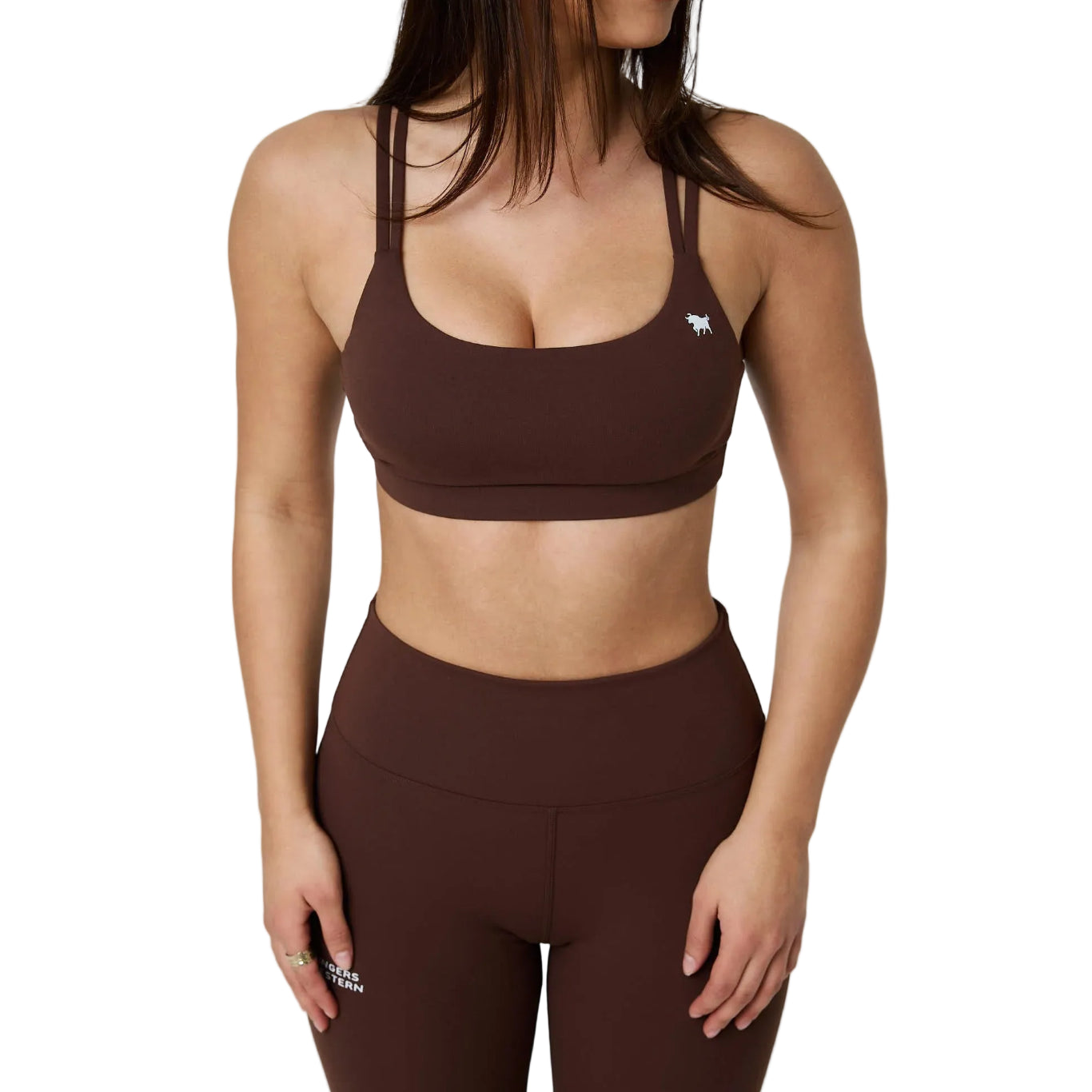 A woman wearing a matching brown activewear set consisting of a scoop-neck sports bra and high-waisted leggings, shown from the chest down against a white  studio background.