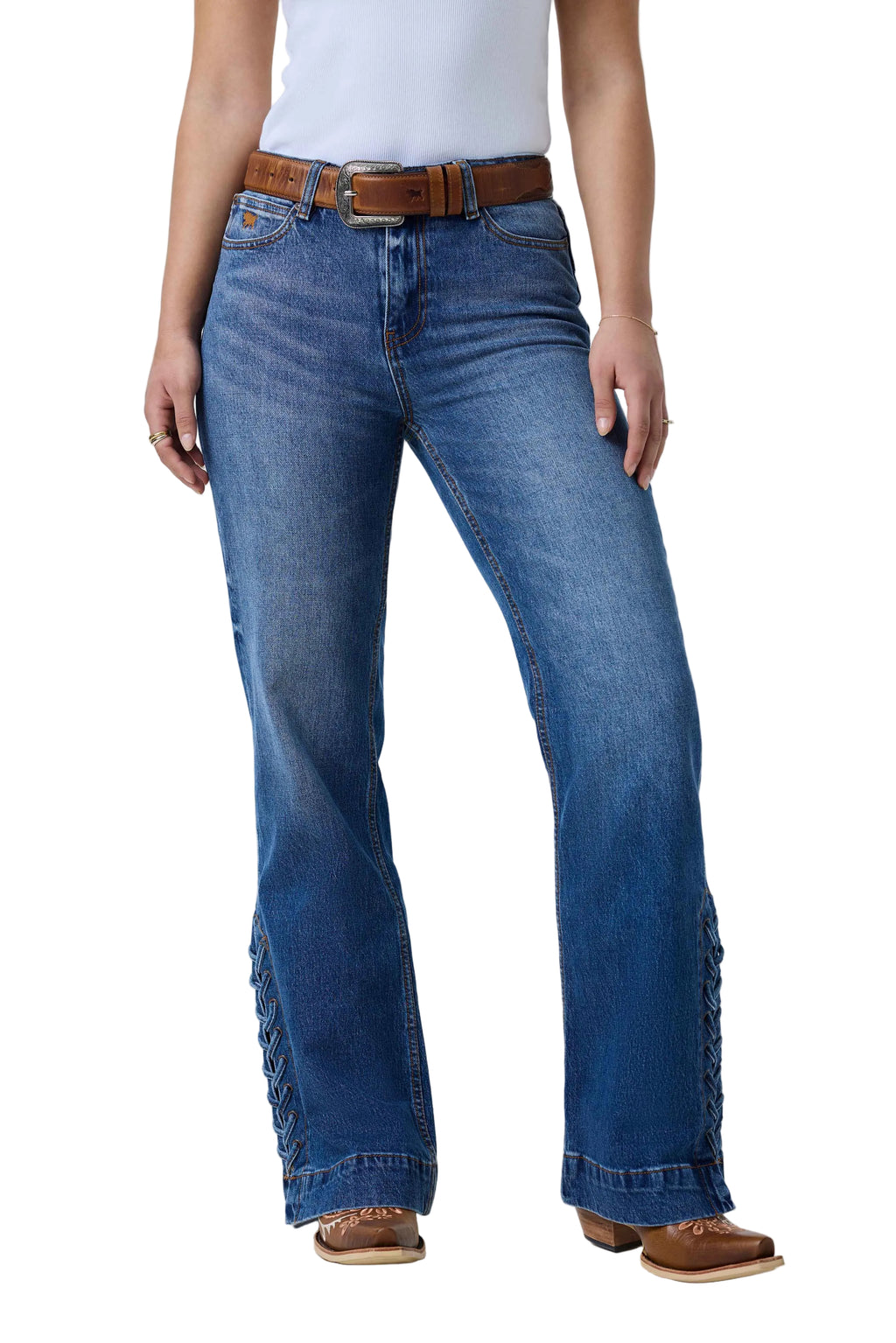 A person wearing blue denim jeans with decorative fringe detailing down the outer sides of the legs, styled with a brown belt, white top, and brown boots against a white studio background.