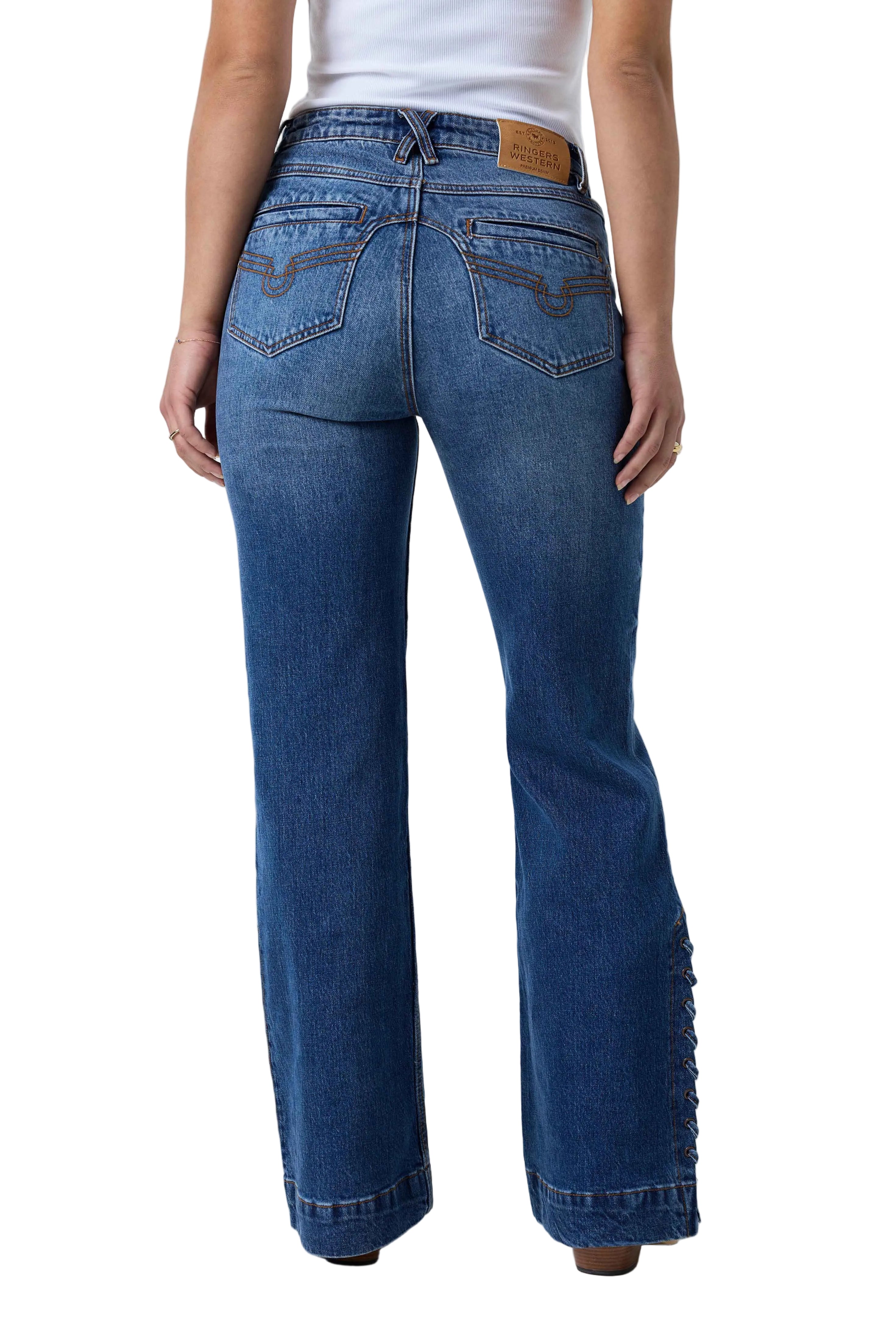A person shown from the back wearing blue denim jeans with a straight-to-flare leg and decorative side cutouts near the hem, paired with a white top against a white studio background.