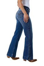 A person wearing blue flare jeans with decorative lace-up detailing down the outer side of the legs, paired with brown cowboy boots against a white studio background.