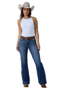 A woman modeling a pair of blue flare jeans with decorative stitching down the outer legs, styled with a white sleeveless top, a brown belt, and a beige cowboy hat against a white studio background.